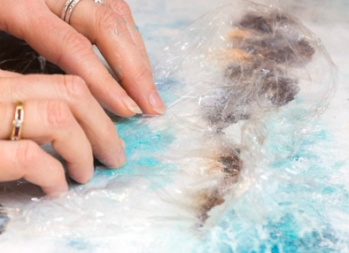 hands showing how to add cling film to a watercolour painting to create patterns of water.